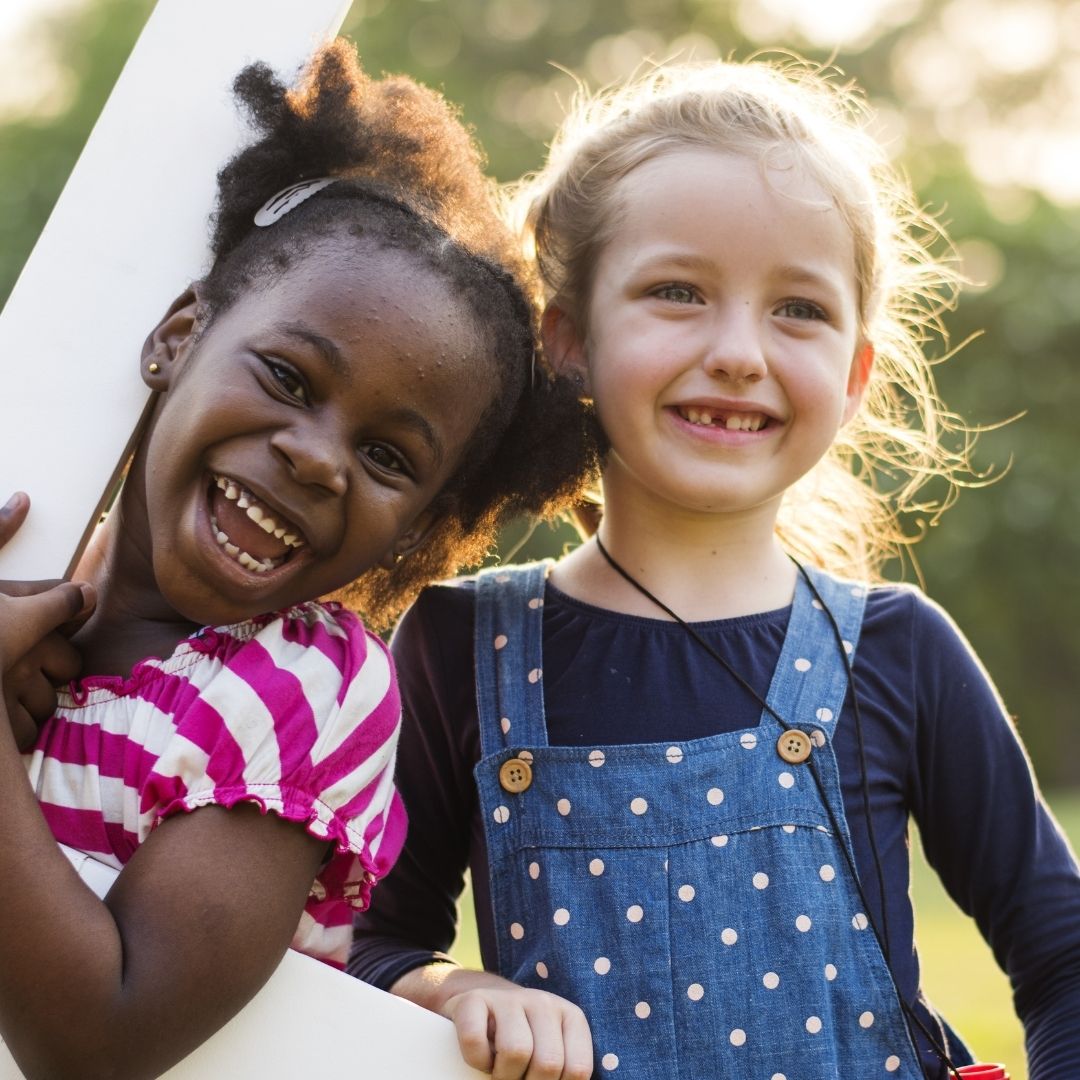 Two diverse young girls smiling and laughing outdoors, illustrating the enhanced social development benefit.