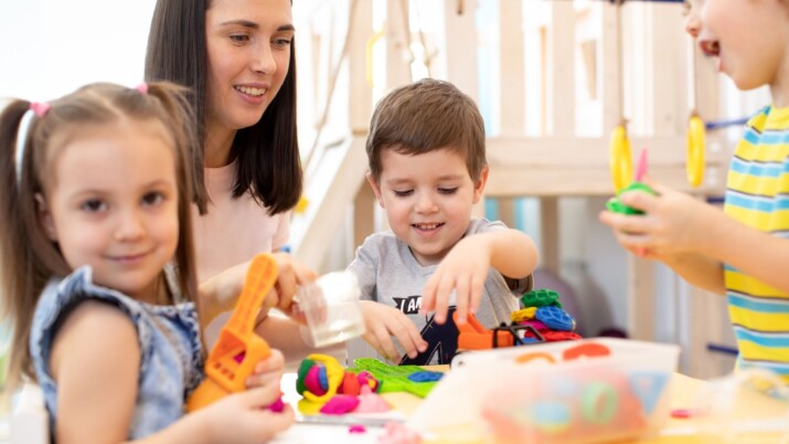 Teacher and children engaging in sensory play with blocks and playdough at a daycare center.